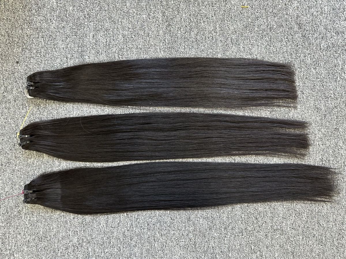 Three straight dark hair wefts laid side by side on a gray carpet
