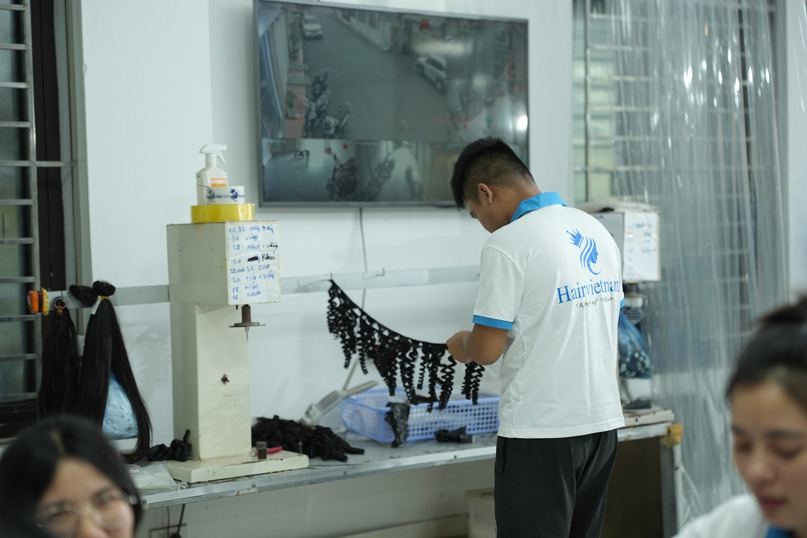 A staff member handles a curly dark hair weft strip hanging over a work table