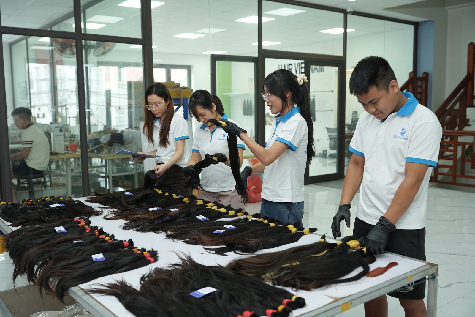 A man in black gloves inspects a long dark hair bundle at a table with other bundles