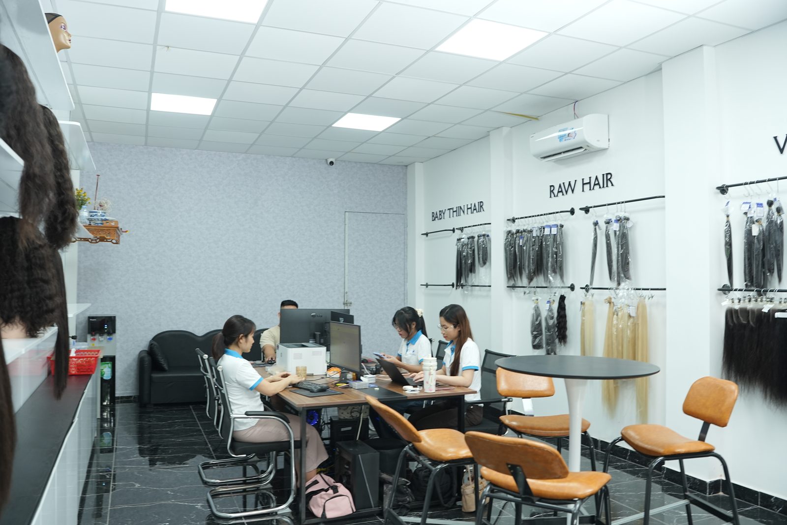 Office with wall displays of hair bundles, desks with staff at laptops and wigs on shelves