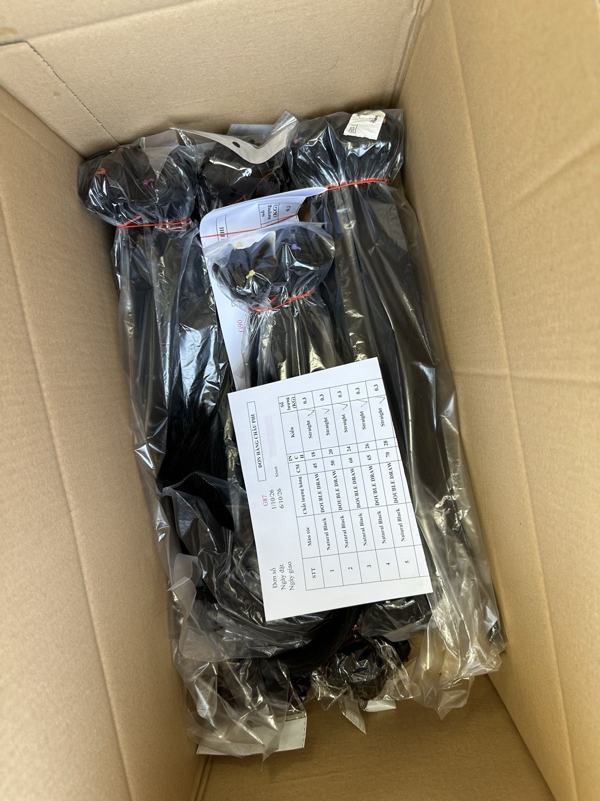 Hair bundles bagged by length in a shipping carton, with a packing list showing color, drawn level, length and weight