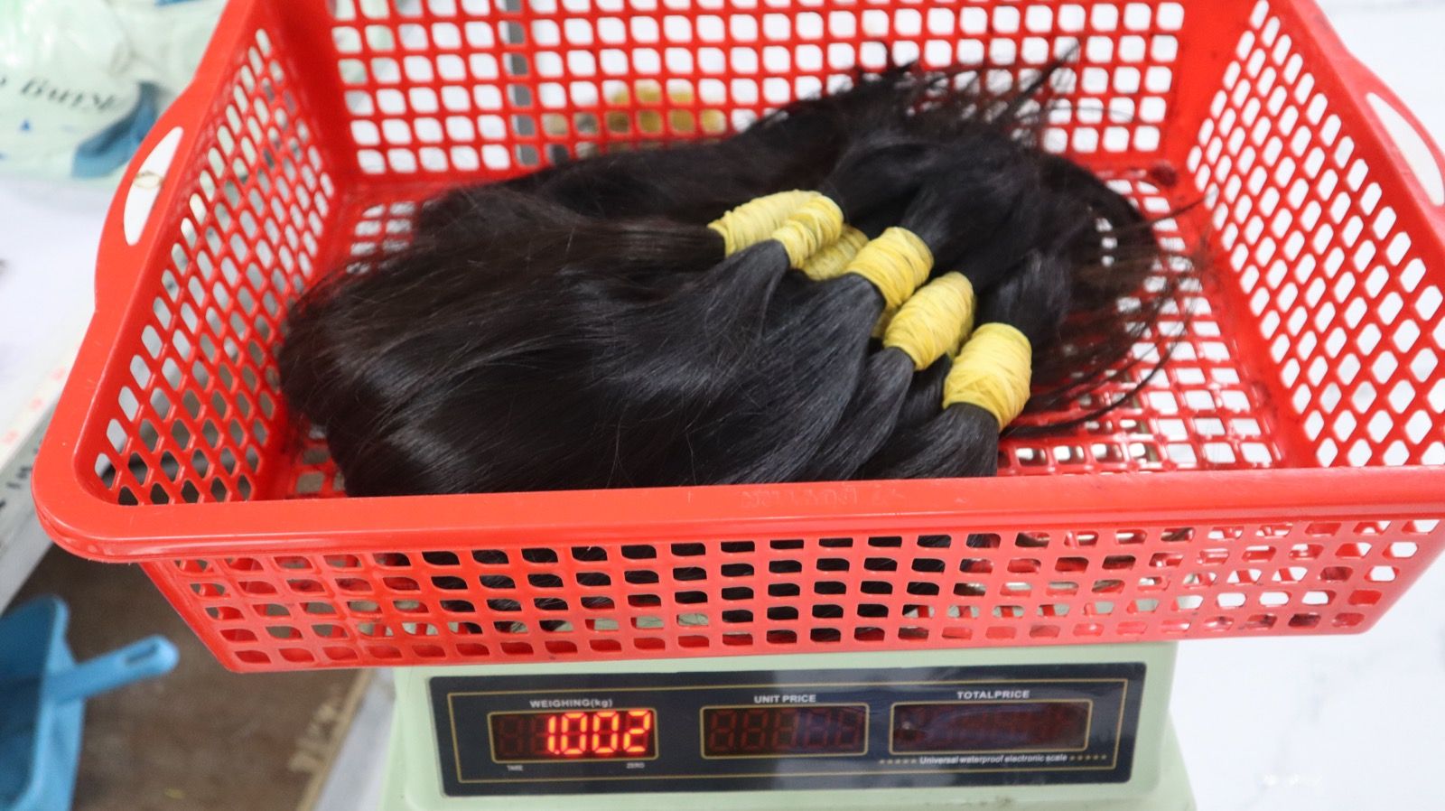 Several tied bundles of bulk hair in a red basket on a digital scale reading 1.002 kg